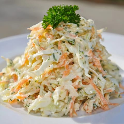Bowl of Coleslaw with Apple topped with fresh parsley, showing creamy dressing clinging to crunchy cabbage and bright apple shreds.