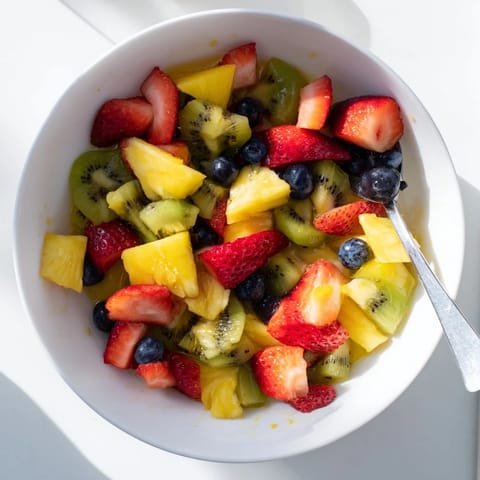 Freshly tossed Fruit Salad filled with juicy pineapple, blueberries, and orange segments, garnished with mint for a refreshing snack.