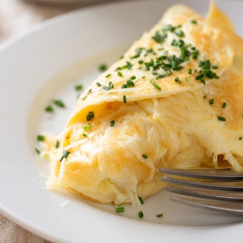 Golden-brown omelet with cheese is garnished with fresh chives on a white plate.