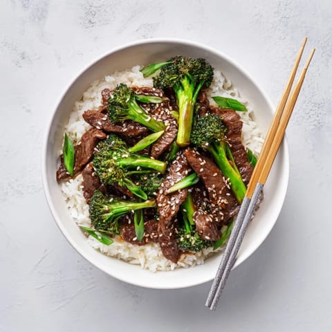 A steaming bowl of homemade Beef and Broccoli stir-fry sits beside fluffy white rice, ready for a delicious weeknight dinner.