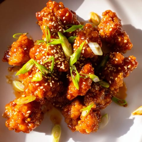 Close-up of homemade Orange Chicken glistening with fresh orange zest, garnished with sesame seeds and vibrant sliced green onions.