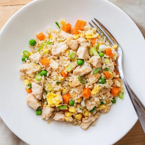 A close-up of vibrant Chicken Fried Rice garnished with fresh green onions, served alongside a small bowl of soy sauce.