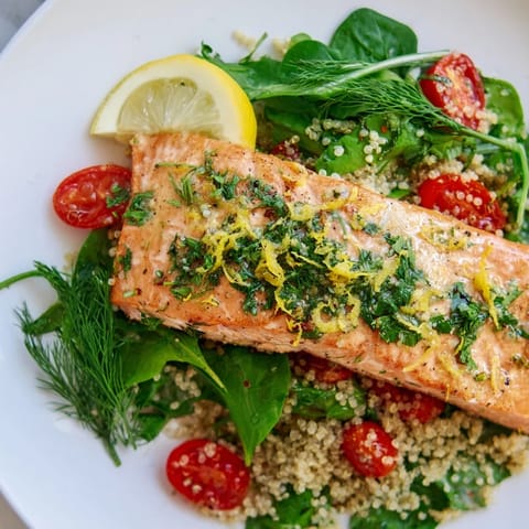 Flaky lemon herb salmon sits on fluffy quinoa and crisp greens, with cucumber slices and a drizzle of zesty citrus dressing.