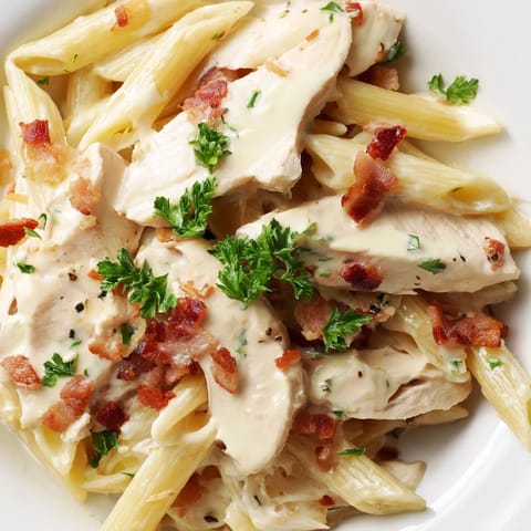 A close-up photo of Creamy Chicken Bacon Penne highlights tender chicken slices and smoky bacon nestled among penne pasta, garnished with fresh parsley.