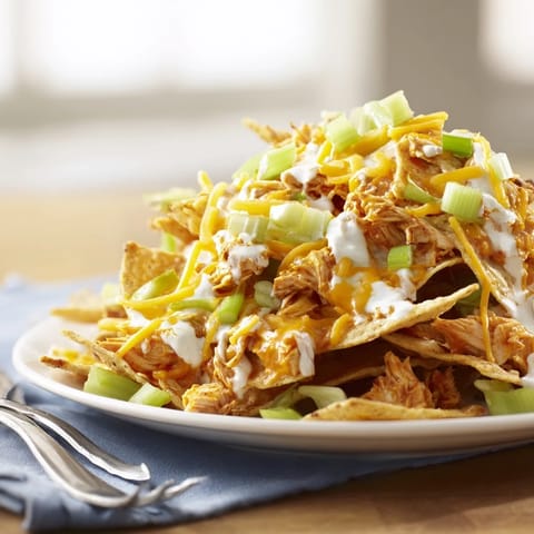 Freshly baked Buffalo Chicken Nachos feature crispy tortilla chips loaded with spicy shredded chicken, melted cheese, and a cool ranch drizzle.