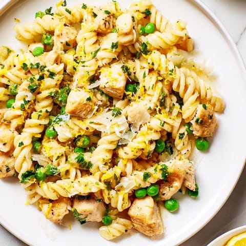 Garlic Butter Chicken & Pea Pasta served family-style in a skillet, garnished with fresh parsley and lemon zest, steaming beside a glass of crisp white wine.
