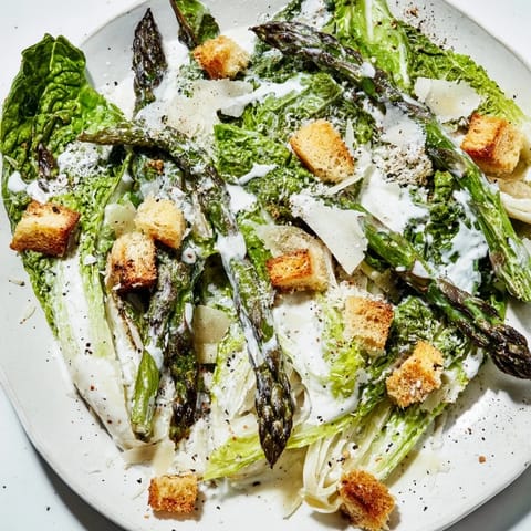 A vibrant bowl of Roasted Asparagus Caesar Salad showcases charred vegetables, shaved Parmesan, and crunchy homemade croutons.  