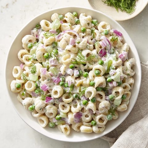 A close-up of Creamy Dill Pickle Pasta Salad shows a creamy, zesty dressing coating the pasta, with visible flecks of celery and red onion.
