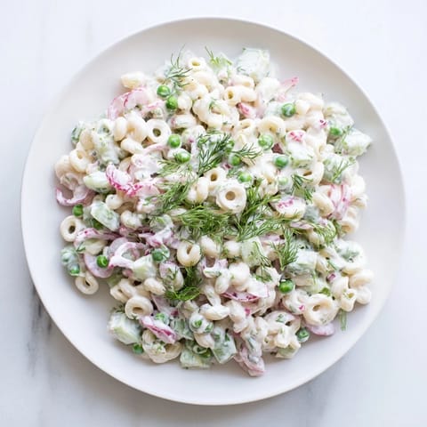 Creamy Dill Pickle Pasta Salad is served chilled in a white bowl, featuring ditalini pasta mixed with diced pickles, peas, and fresh herbs.