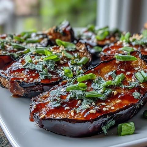 Roasted miso glazed eggplant halves glisten with a caramelized glaze, topped with green onions and sesame seeds.