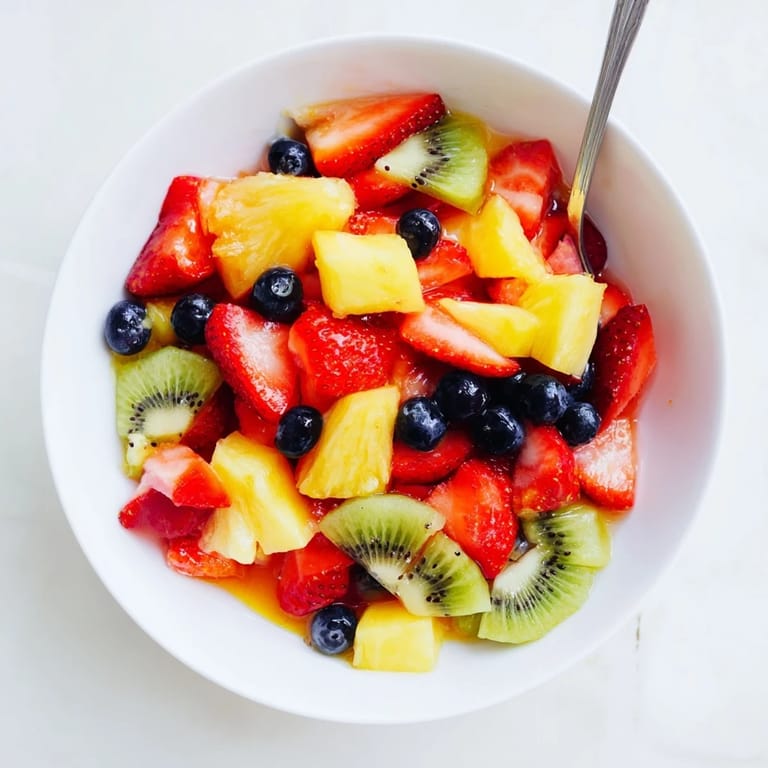 Healthy vegan Fruit Salad mixed with strawberries, grapes, and kiwi, lightly coated in a sweet citrus syrup on a white plate.