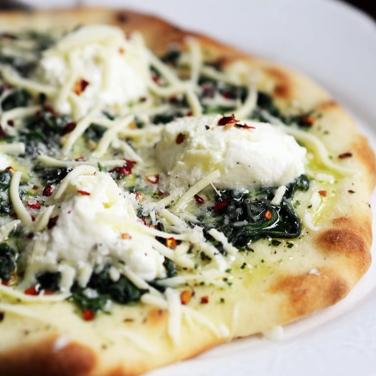 A freshly baked Spinach Ricotta Pizza is sliced to reveal its thin, crispy crust and garlic butter base.