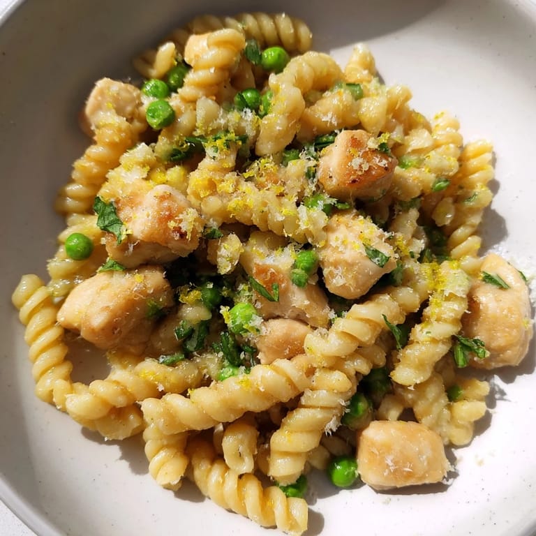 A generous bowl of Garlic Butter Chicken & Pea Pasta topped with shaved Parmesan and a lemon wedge, ready for a comforting, weeknight family dinner.
