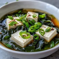 Steaming bowl of wakame soup with silken tofu and sliced scallions in delicate dashi broth.