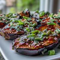 Roasted miso glazed eggplant halves glisten with a caramelized glaze, topped with green onions and sesame seeds.