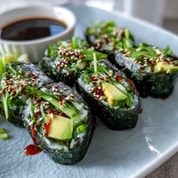 Eight homemade Nori Rolls with Vegetables arranged on a bamboo mat, filled with crisp cucumber, creamy avocado, and crunchy sprouts for dipping.