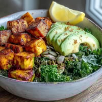 Golden, crispy tofu and sautéed kale topped with creamy avocado slices and a lemon wedge in a breakfast bowl.
