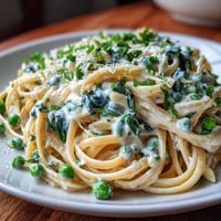 Creamy spring pasta with lemon sauce and peas in a skillet, garnished with Parmesan and lemon zest.